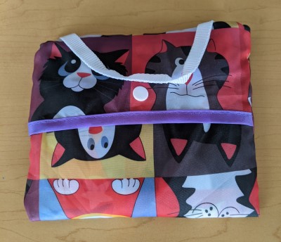 A folded nylon tote with a snapper and carrying handle with a cute cat print